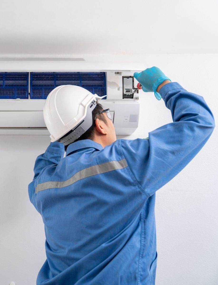 A man wearing a hard hat and gloves is working on an air conditioner.